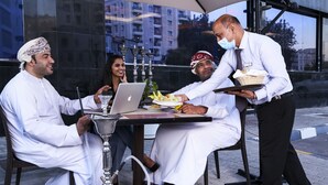 A group of people seated around a table with a laptop, a glass, and a traditional drink set. - Garden Hotel Muscat (Muscat)