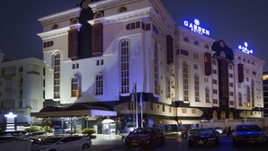 A large hotel with a prominent "GARDEN" sign, multiple entry points, and a parking area with several cars. - Garden Hotel Muscat (Muscat)
