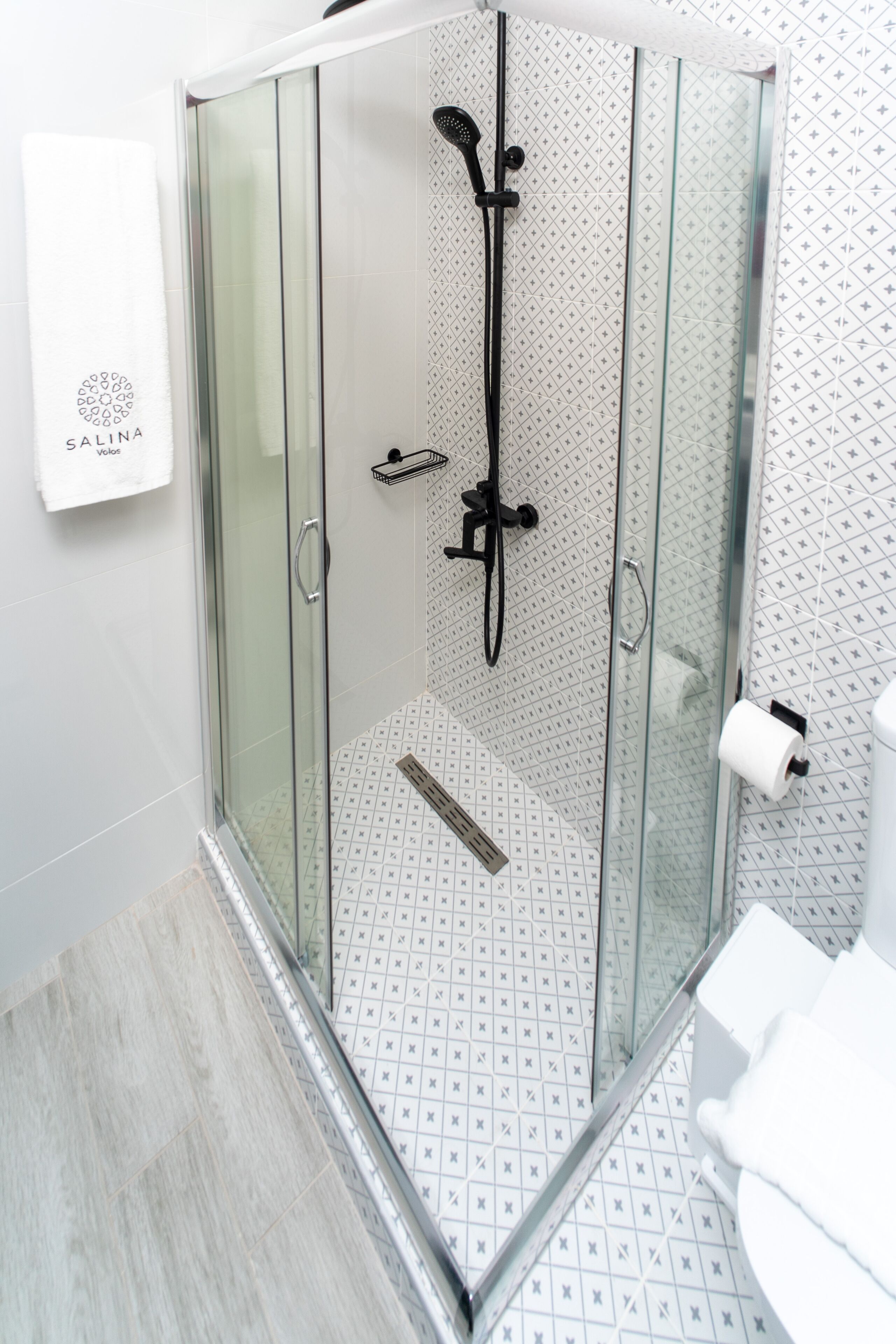 Un bagno moderno con doccia vetro e pareti piastrellate di bianco, con un asciugamano bianco appeso al muro.
