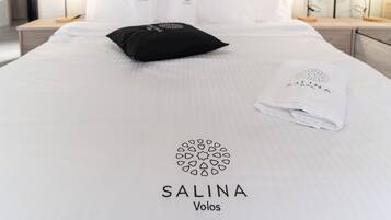 Een net opgemaakt bed met een witte spreidek die een logo en de naam 'SALINA Volos' in het midden heeft.