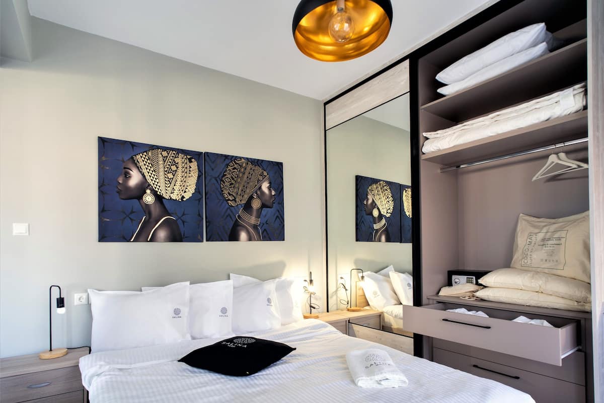 A modern hotel room with a large bed, a bedside table, a nightstand, a wardrobe, and a mirror.