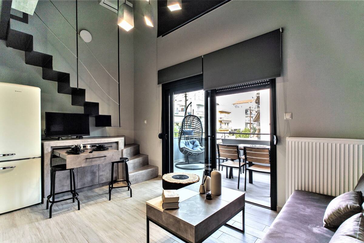 A modern kitchen with a built-in fridge, a dining area with a sofa and a table, and a staircase leading to an outdoor seating area.