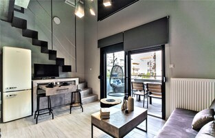 Una cocina moderna con refrigerador integrado, un área de comedor con sofá y mesa, y una escalera que conduce a un espacio exterior con asientos.