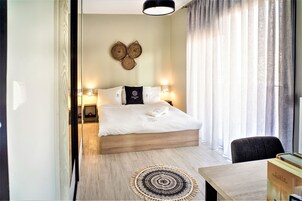 Una habitación de hotel moderna con una cama grande, lámparas de noche, una mesita y vistas al exterior a través de cortinas translúcidas.