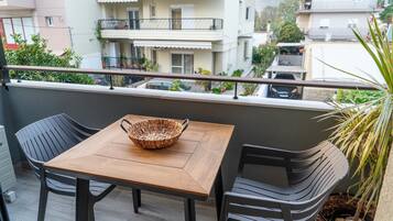 A balcony with a wooden table and two chairs, a woven basket on the table, and a potted plant.