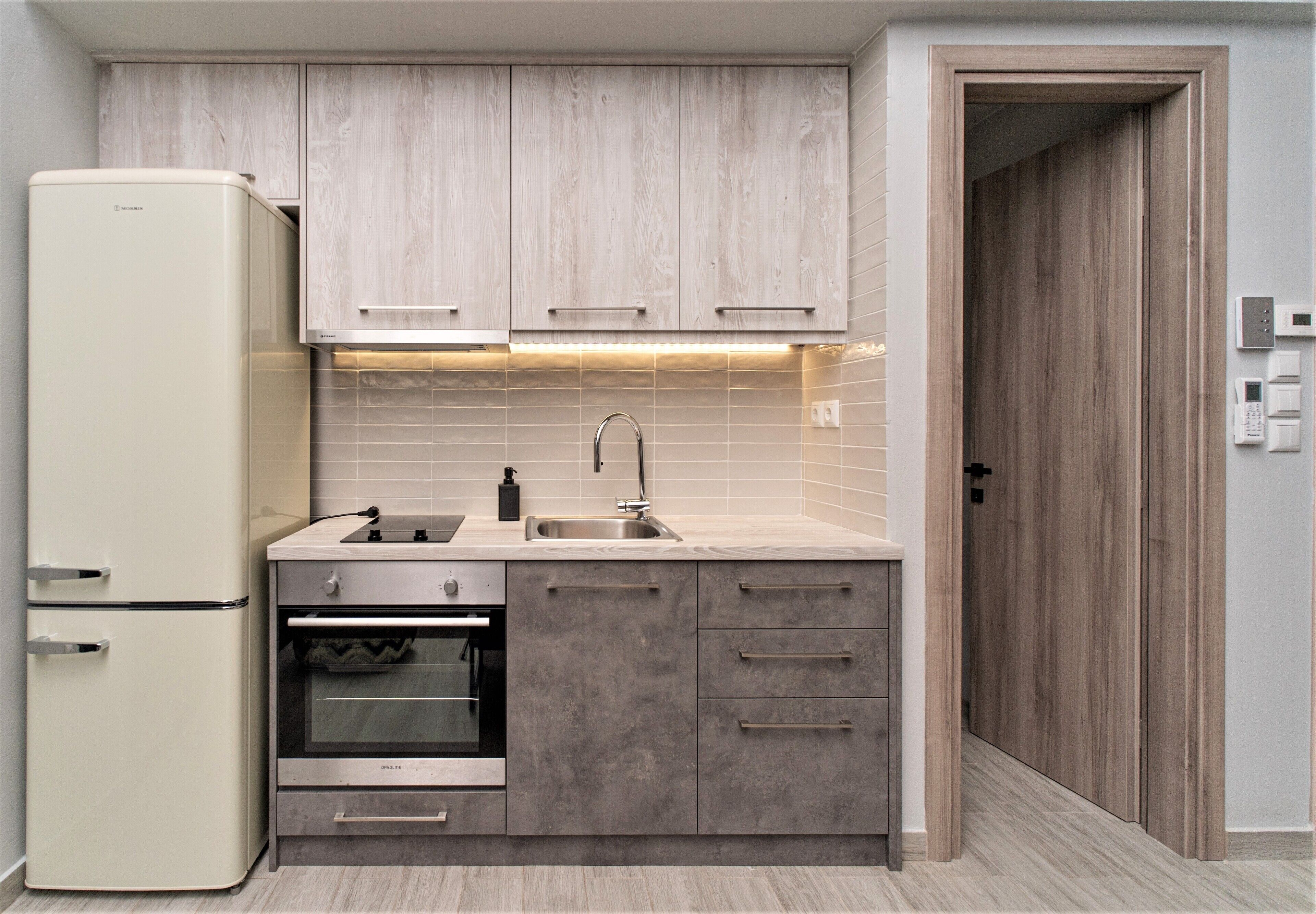 Una cocina compacta equipada con refrigerador, horno, pileta y gabinetes de madera.