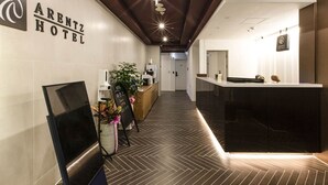 Zona de recepción de un hotel con diseño moderno, que incluye un mostrador, una pantalla digital y una planta.