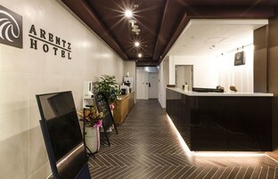 Uma área de recepção de hotel com design moderno, incluindo um balcão, uma tela digital e uma planta.