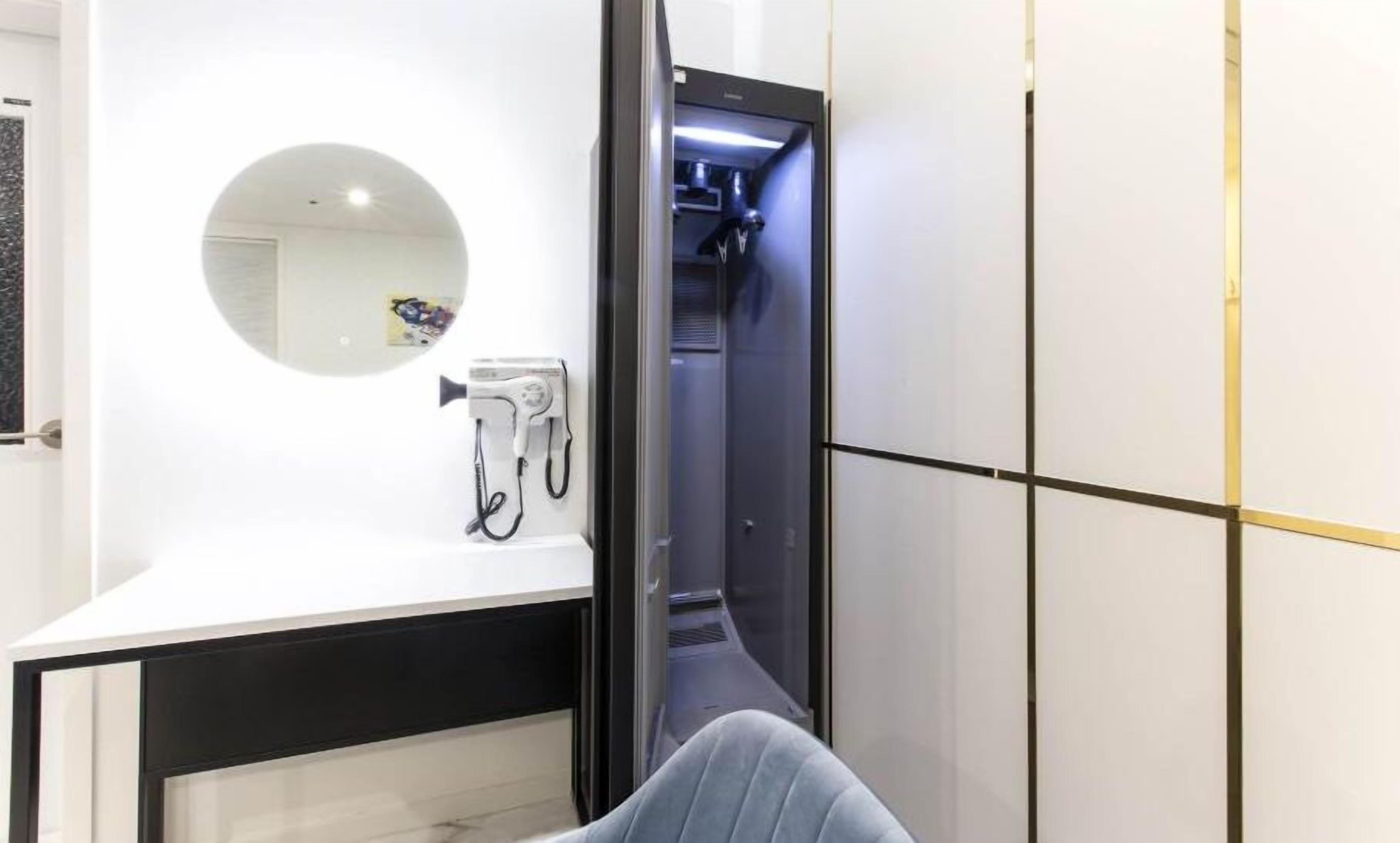 Ein Hotelzimmer mit einem weißen Schminktisch, einem Spiegel, einem Föhn und einem schwarz-goldenen Kleiderschrank.