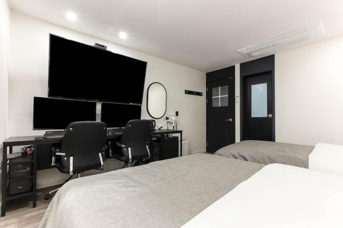 A hotel room with a bed, a desk with two chairs, a television, a mirror, and a door.