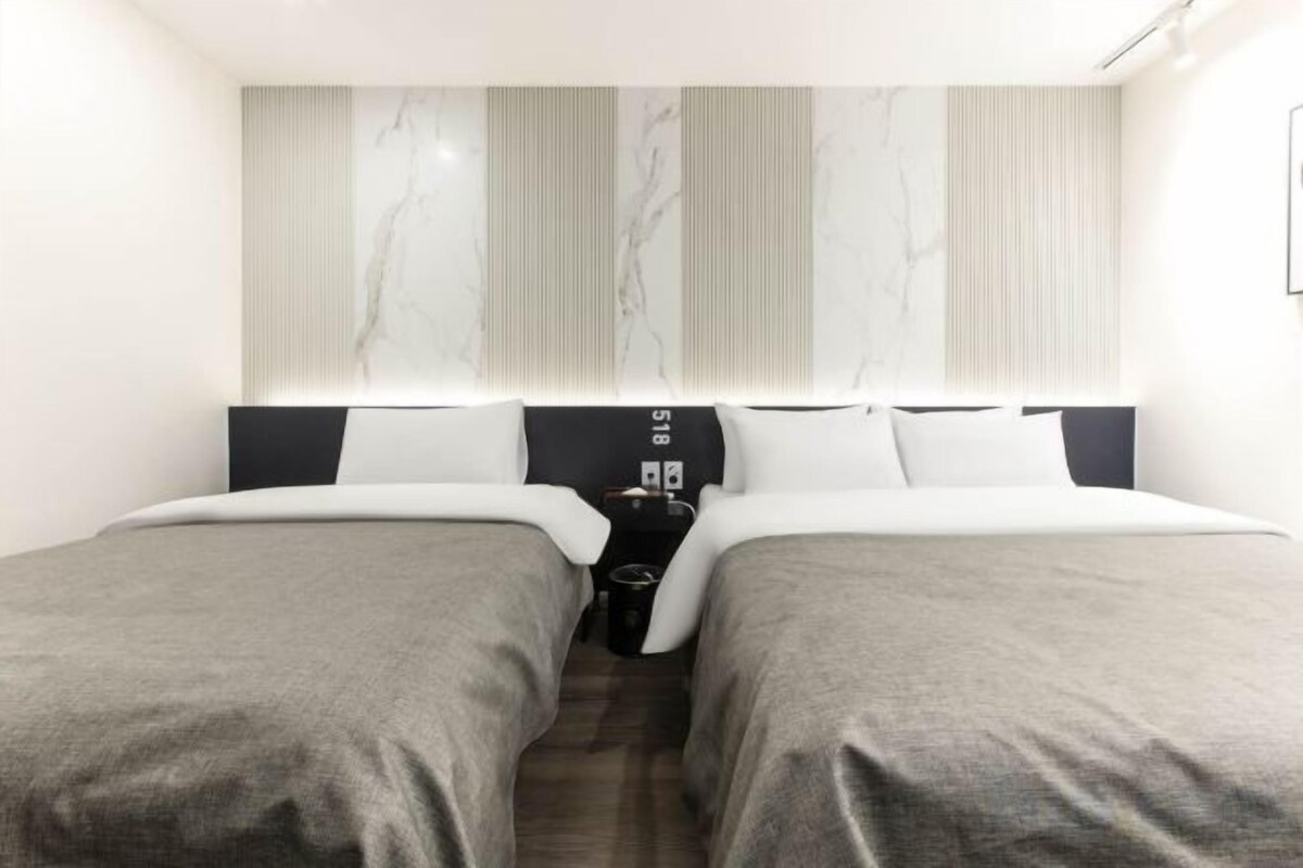 A hotel room with two beds, a nightstand, and a marble-patterned headboard.