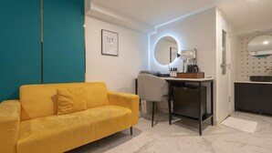 Una habitación moderna con un sofá amarillo, un escritorio con espejo y una pequeña cocina.
