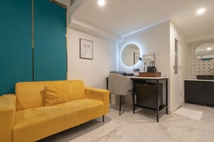 Quarto moderno com sofá amarelo, uma escrivaninha com espelho e uma pequena cozinha compacta.