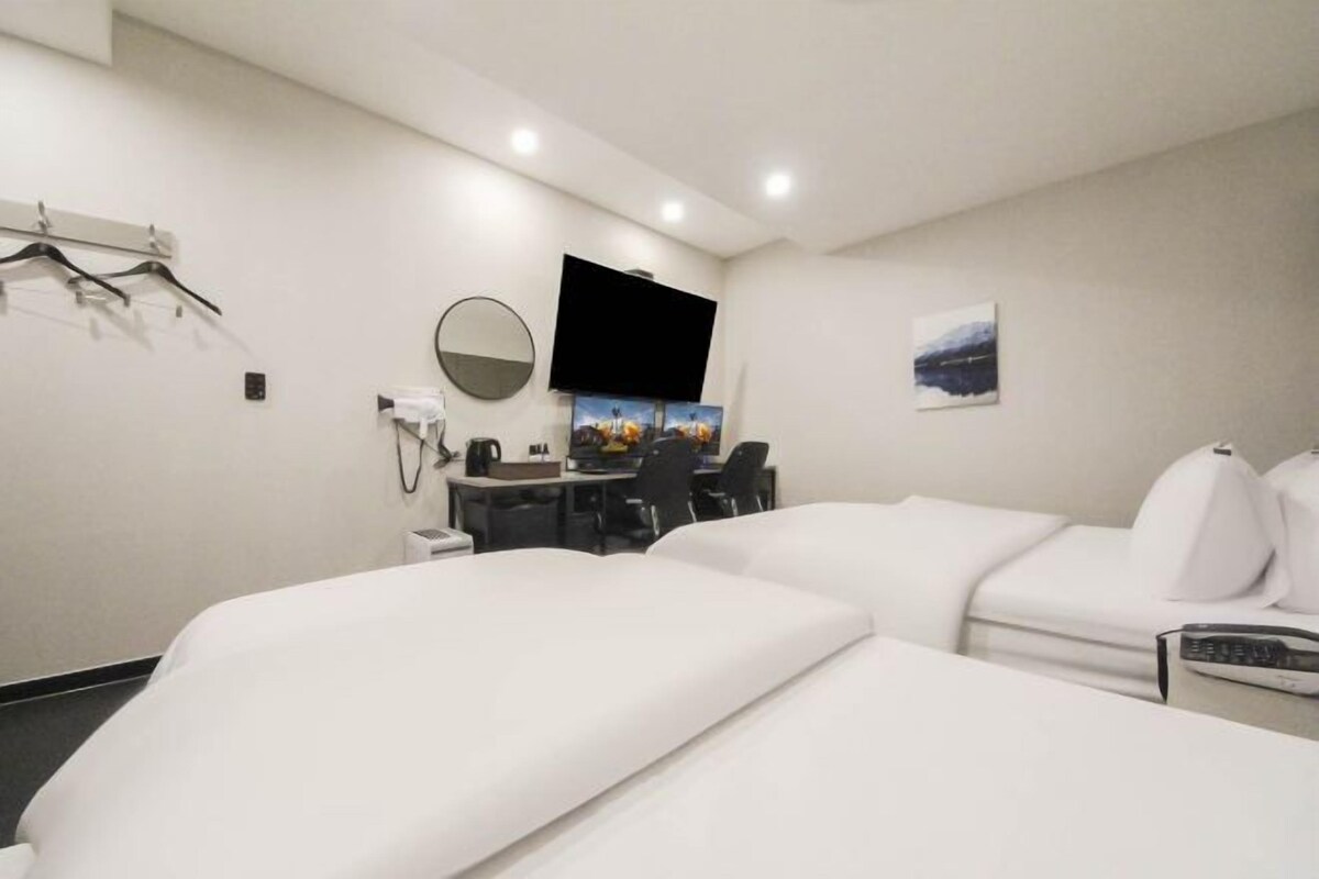 A hotel room with two beds, a desk with a chair, a flat-screen TV, a mirror, and a small table with a coffee maker.