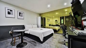 Una habitación de hotel moderna con una cama, una mesita, una silla, un escritorio con una computadora y un espejo grande.