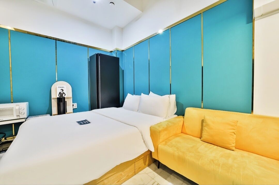 Una habitación de hotel con una cama, un sofá amarillo, un armario negro y un microondas blanco.