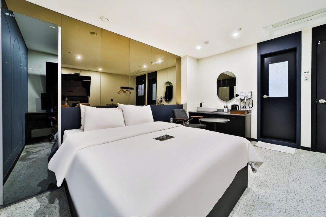 Una habitación de hotel con una cama grande, un escritorio con silla, un espejo redondo, un lavamanos pequeño y un armario.