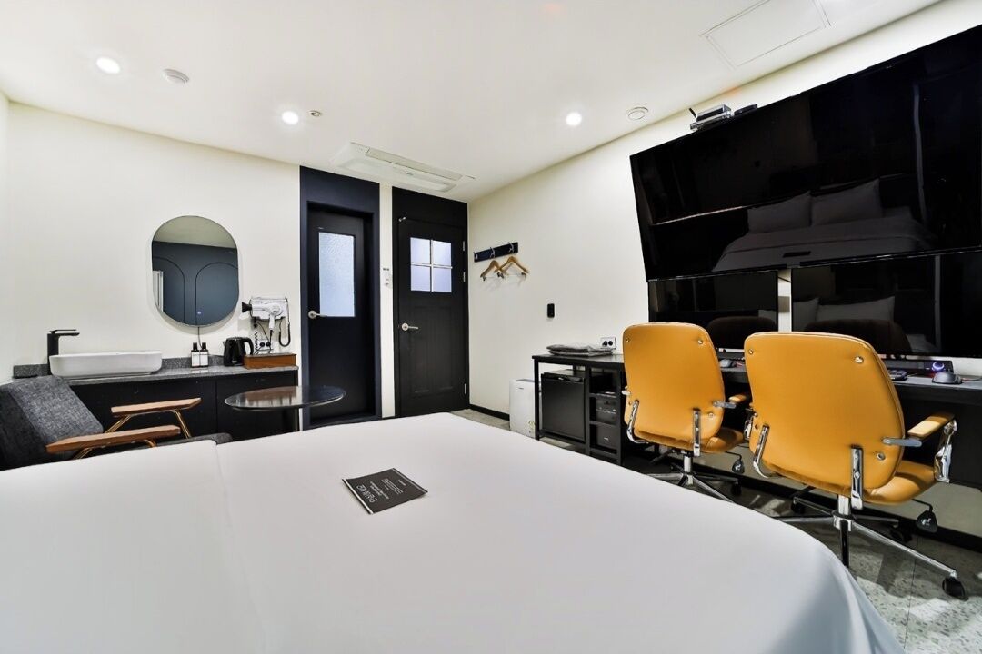 A conference room with a large table, two yellow chairs, a black door, and a black cabinet with a sink.