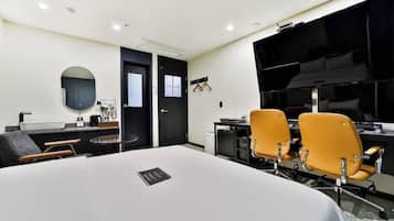A conference room with a large table, two yellow chairs, a black door, and a black cabinet with a sink.
