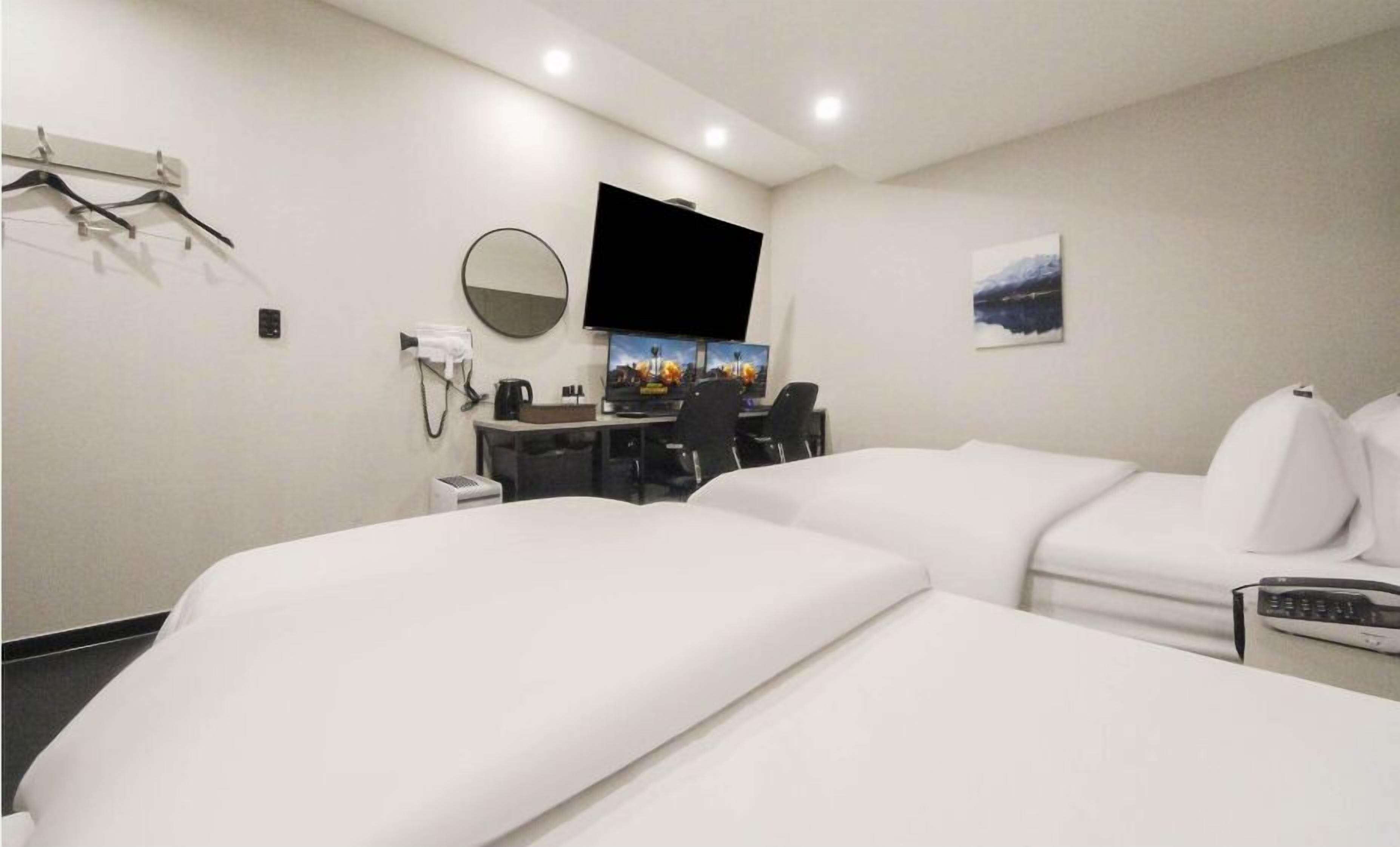 A hotel room with two beds, a desk with a computer, a flat-screen TV, a coffee maker, and a painting on the wall.