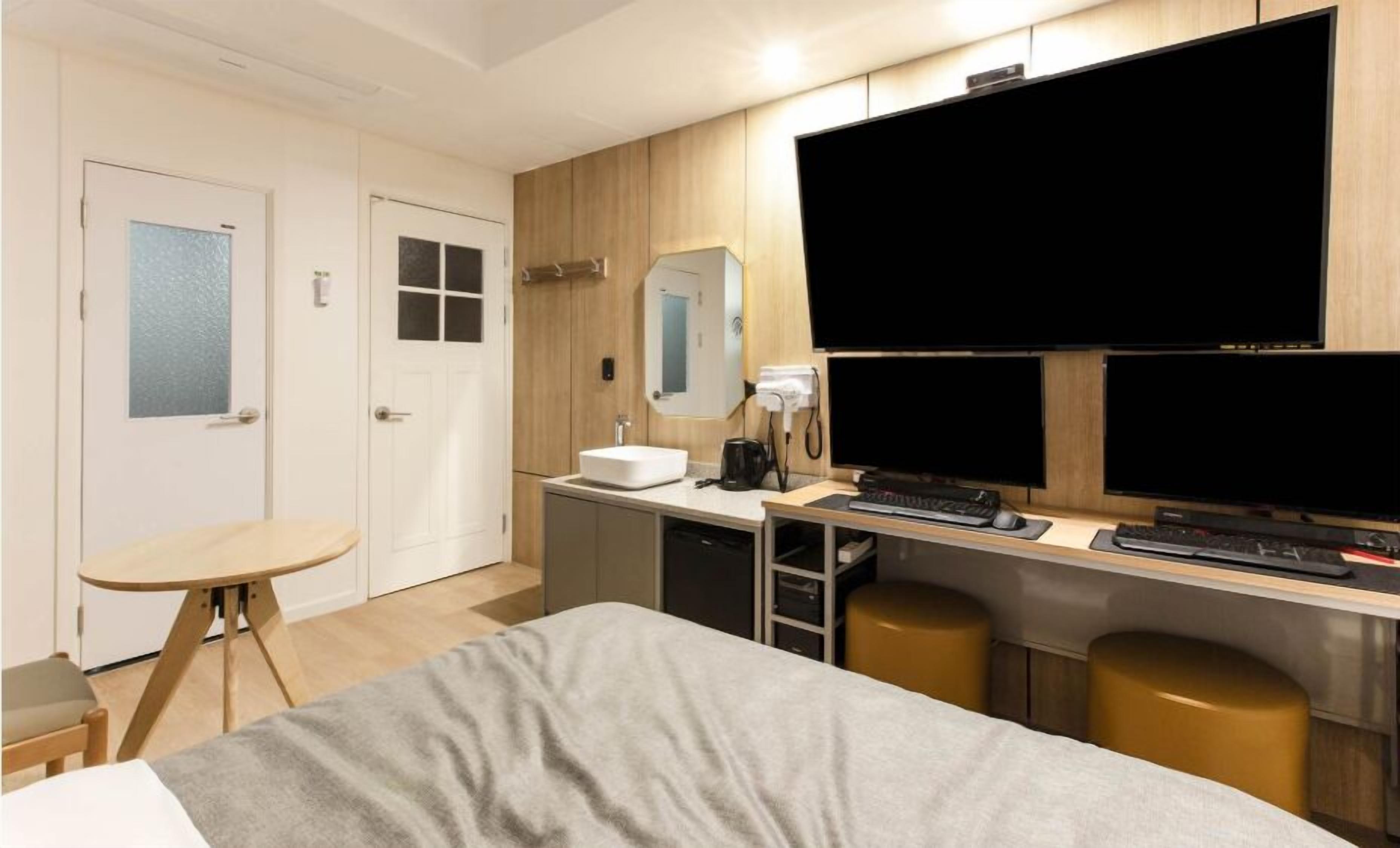 A hotel room with a bed, a desk with a computer, a TV, and a small table.