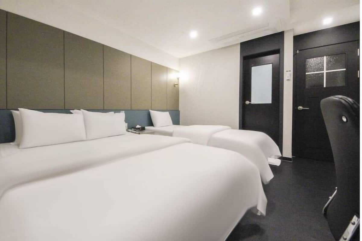 A hotel room with two beds, a dark door, and a light-colored wall.
