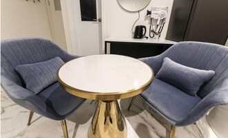Quarto com duas poltronas azuis e uma mesa redonda com base dourada.