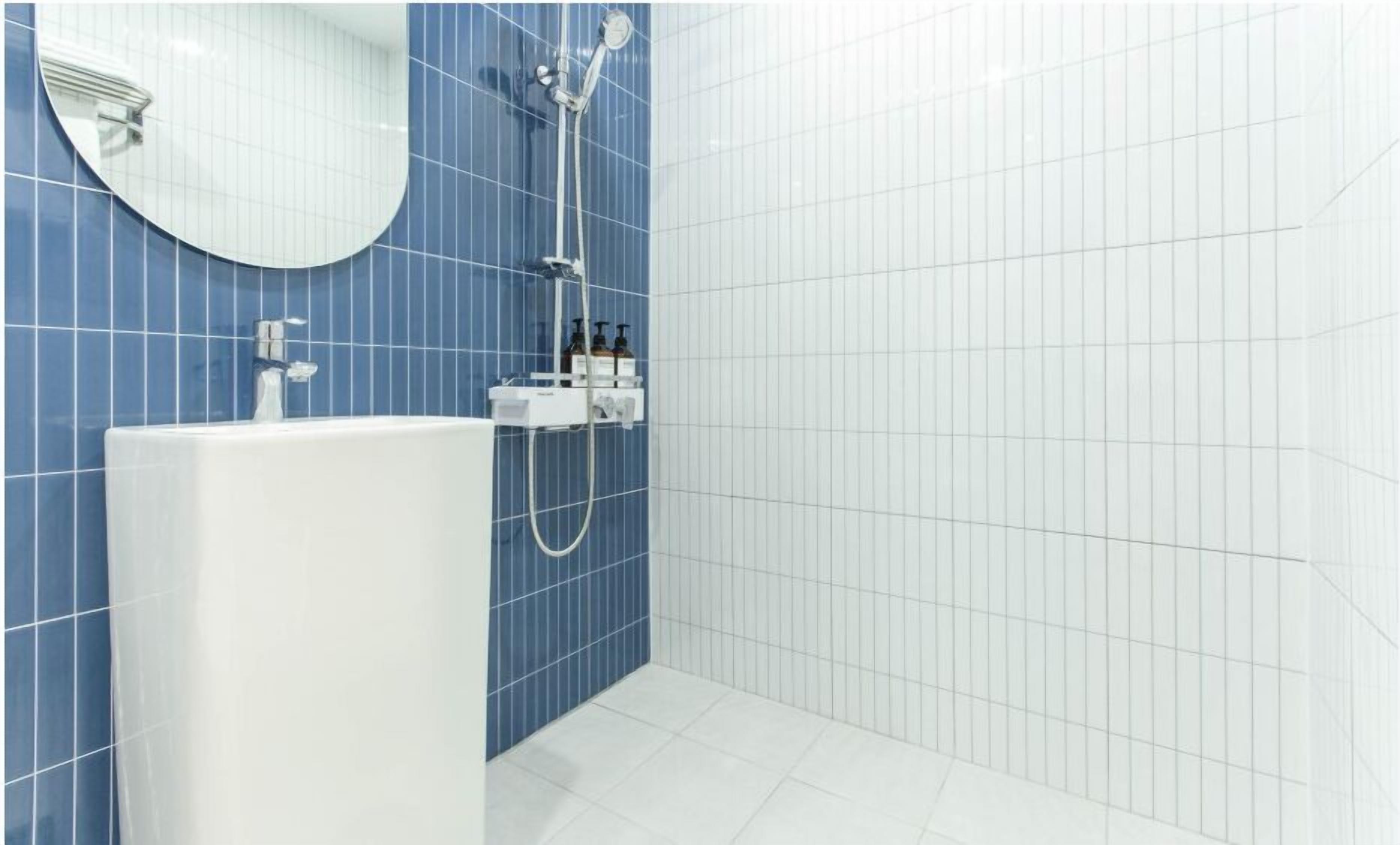 A bathroom with a white bathtub, a round mirror, and a shower with a handheld showerhead.