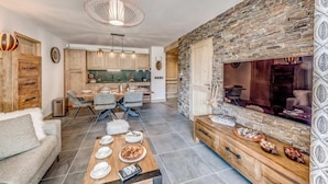 Un salon moderne avec un mur d’accent en pierre, un coin repas avec une table et des chaises en bois, et une cuisine avec des armoires en bois et des luminaires suspendus.