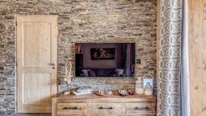 Une pièce avec un mur en pierre, une armoire en bois, un téléviseur à écran plat et un rideau à motifs.