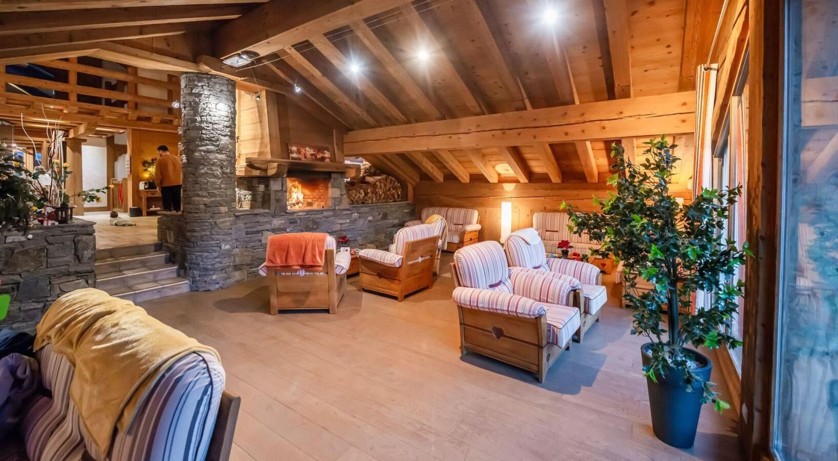Interior acogedor de una cabaña de troncos con chimenea de piedra, muebles de madera y una planta grande en maceta.