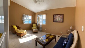 Una sala de estar con un sofá, sillones, una mesita de centro y vista al mar a través de las ventanas.