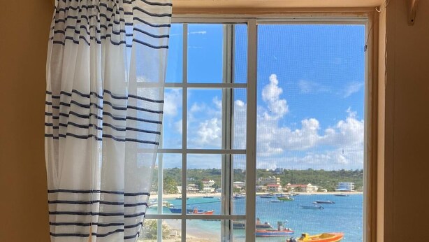 Una habitación con vista al mar y a barcos a través de una ventana con cortina a rayas.