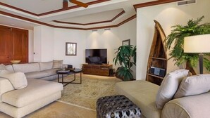 Un salon comprenant un canapé, un pouf, une télévision et un meuble en bois.