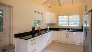 Una cocina moderna con armarios blancos, encimera negra, electrodomésticos de acero inoxidable y una ventana con persianas.