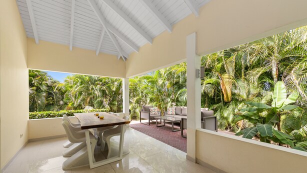 Amplia habitación con comedor, sofá y vistas a exuberante follaje tropical.