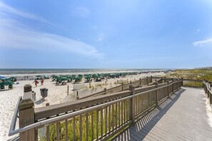 A beach with a wooden boardwalk, umbrellas, and beachgoers.