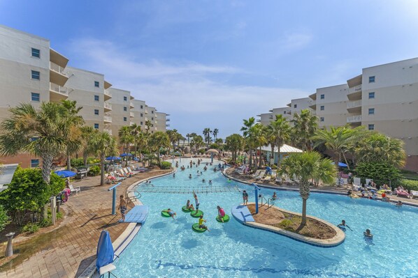A large indoor swimming pool surrounded by palm trees and lounge chairs, with multiple levels of white buildings in the background.