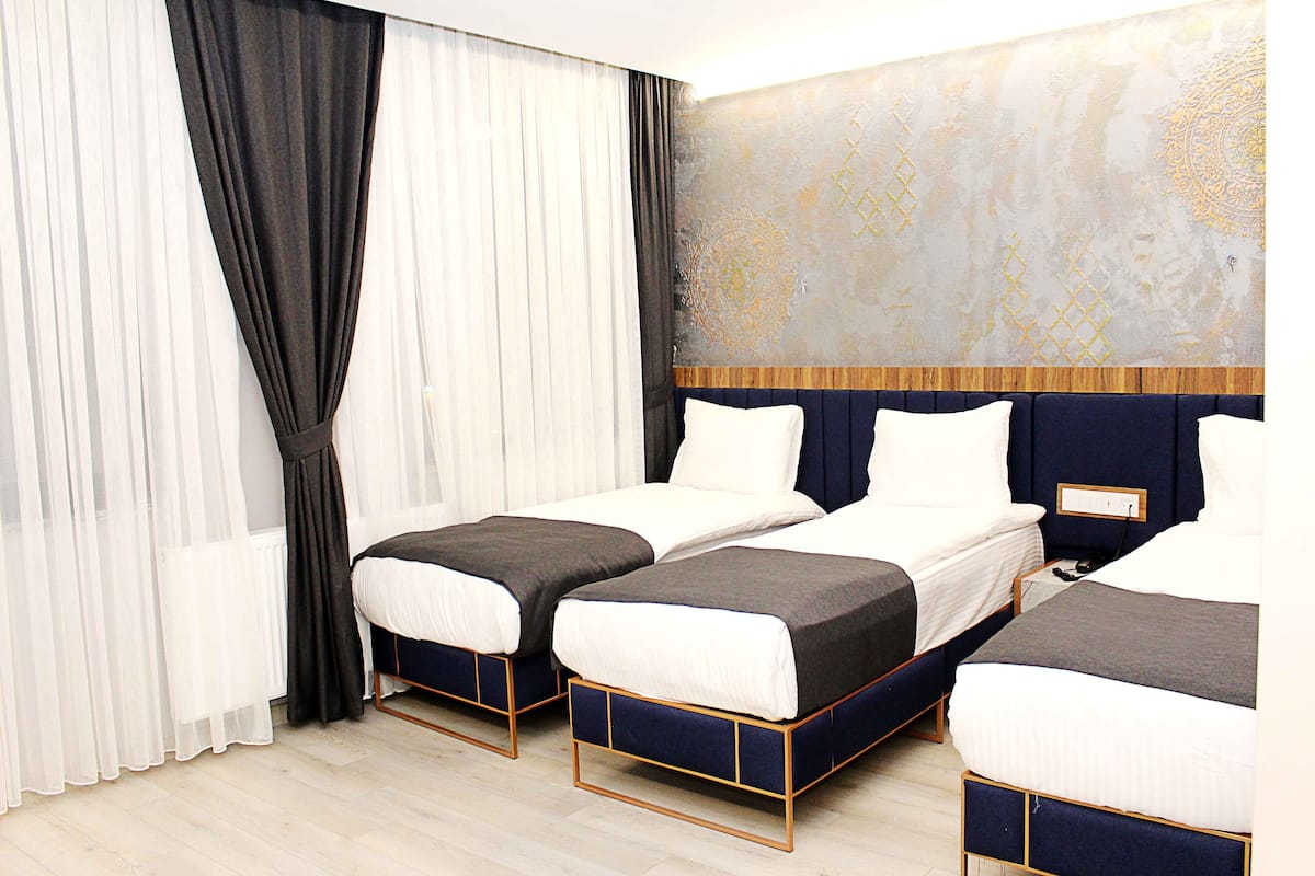 A hotel room with two single beds, a large abstract wall mural, and sheer curtains.