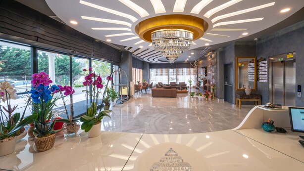 A modern lobby with a chandelier, potted plants, a reception desk, and a seating area. - Seyithan Palace Hotel  (Istanbul)
