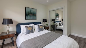 A bedroom with a bed, two bedside tables with lamps, a large mirror, and a painting on the wall. - Captivating 3-bed Apartment by Gleneagles (Auchterarder)