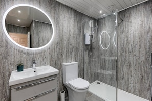 A modern bathroom with a round mirror, white fixtures, and a shower enclosure. - Captivating 3-bed Apartment by Gleneagles (Auchterarder)