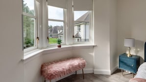 A room with a bay window, a bench, a small table with a lamp, and a blue cabinet. - Captivating 3-bed Apartment by Gleneagles (Auchterarder)