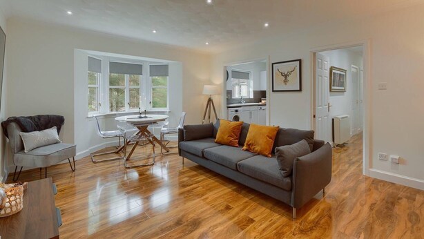 A modern living room with a grey sofa, wooden flooring, and a dining table with chairs. - Captivating 3-bed Apartment by Gleneagles (Auchterarder)