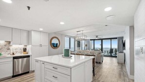 A modern kitchen with white cabinetry, a central island, and a dining area with a view.