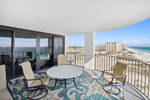 A balcony with a view of the beach and ocean, furnished with chairs and a table.