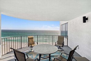 A balcony with a round table and four chairs, overlooking a beach and the ocean.