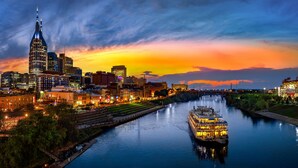 A riverboat in a city with a prominent skyscraper and a sunset. - Music City Retreat (Nashville)