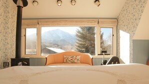 Een slaapkamer met een groot bed, een raam met uitzicht op de bergen, een open haard en een nachtkastje.