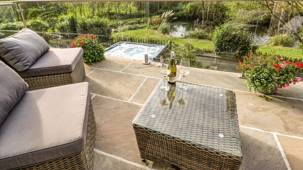 A balcony with wicker furniture, a hot tub, and a view of a river and greenery. - Belvedere Farm (Halifax)